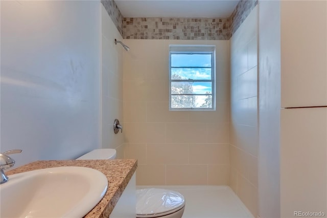 bathroom with sink, tiled shower, and toilet