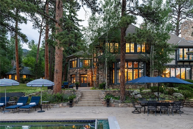 rear view of house featuring stone siding, an outdoor pool, and a patio