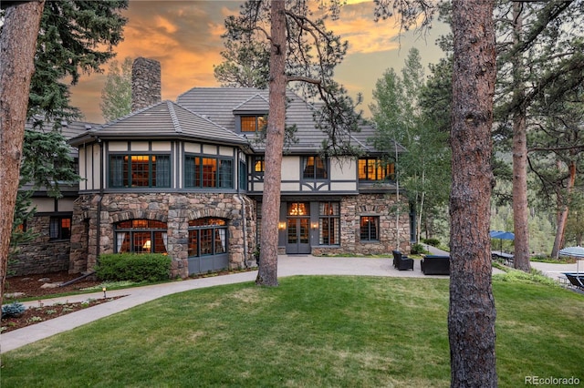 back of property featuring stucco siding, a lawn, stone siding, french doors, and a chimney