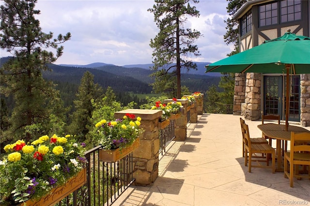 view of patio / terrace with a wooded view, outdoor dining area, and a mountain view