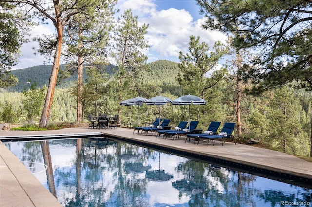 pool with a mountain view, a view of trees, and a patio