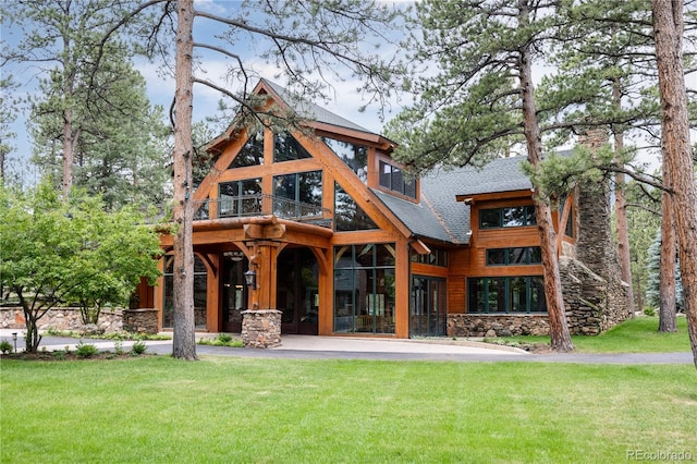 rear view of property with a balcony, a yard, and stone siding