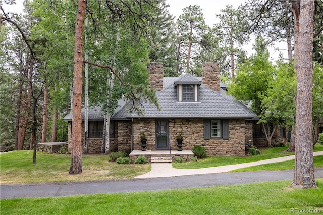 view of front of property featuring stone siding, a chimney, and a front yard