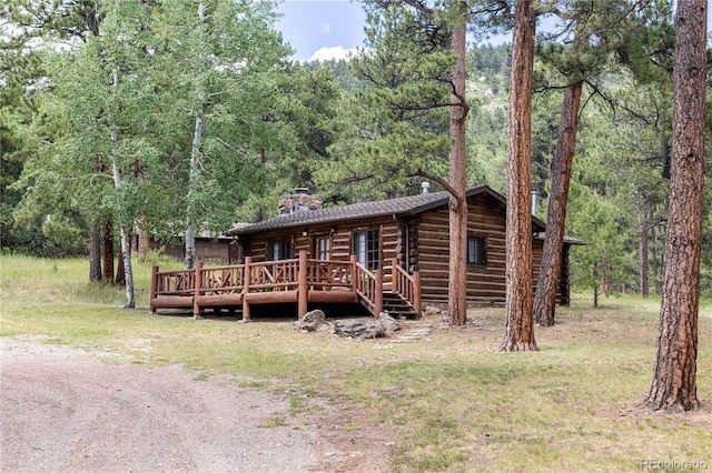 log cabin with a wooden deck, log exterior, a view of trees, and a chimney