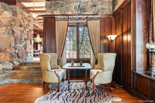 sitting room with an inviting chandelier, wooden walls, and wood finished floors