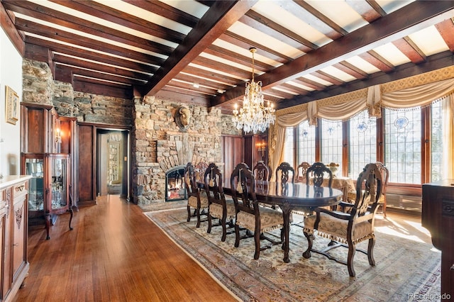 dining space featuring a stone fireplace, plenty of natural light, dark wood-type flooring, and an inviting chandelier