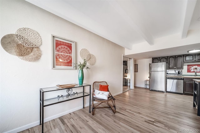 interior space featuring baseboards, beamed ceiling, light wood-type flooring, light countertops, and stainless steel appliances