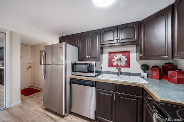 kitchen featuring dark brown cabinets, baseboards, light wood-type flooring, stainless steel appliances, and a sink