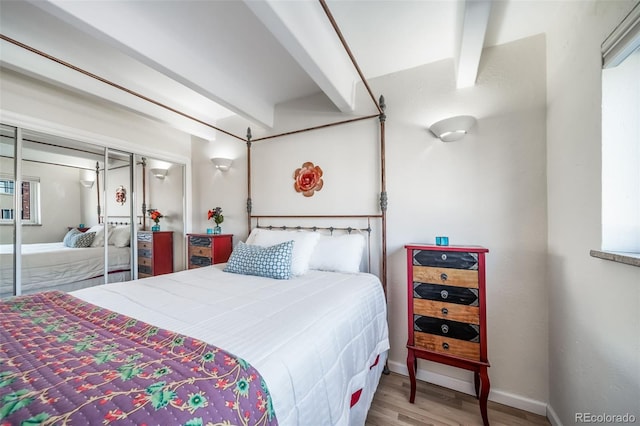 bedroom with a closet, beamed ceiling, baseboards, and wood finished floors