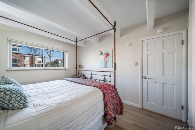 bedroom with baseboards, beam ceiling, and wood finished floors