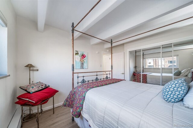 bedroom with beam ceiling, wood finished floors, baseboards, and a closet