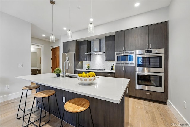 250 Columbine St Unit 310, Denver, CO 80206 - kitchen with wall chimney range hood, appliances with stainless steel finishes, light wood-type flooring, a kitchen bar, and recessed lighting