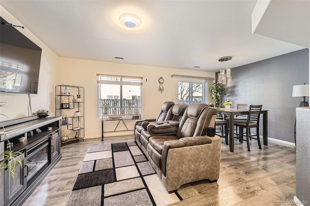 living room featuring light wood-style floors, visible vents, a chandelier, and baseboards