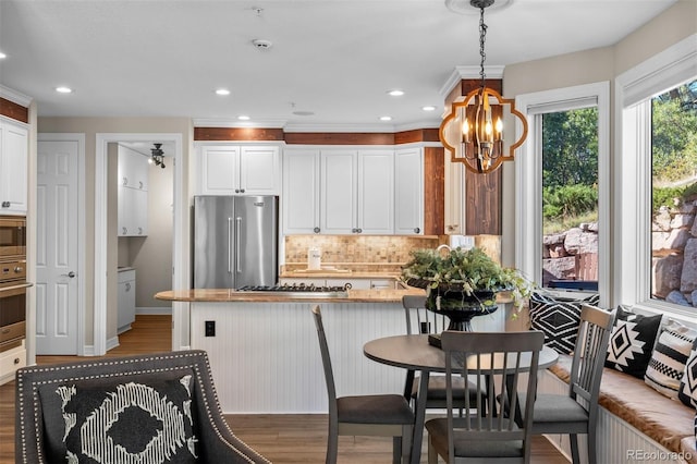 kitchen featuring white cabinetry, hardwood / wood-style floors, stainless steel appliances, decorative backsplash, and hanging light fixtures