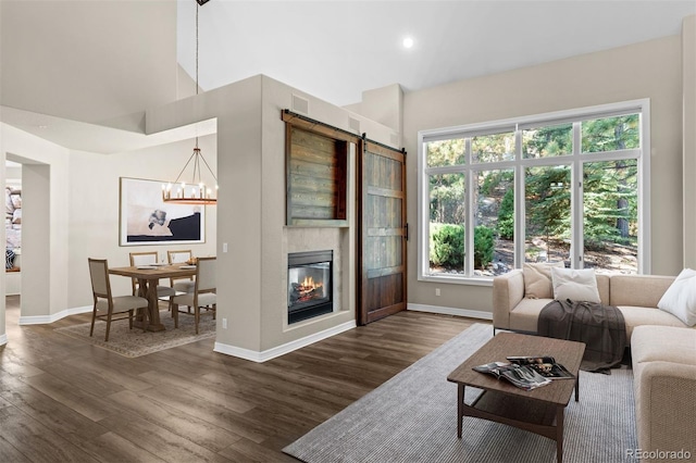 living room with a large fireplace, dark hardwood / wood-style flooring, a barn door, and a notable chandelier