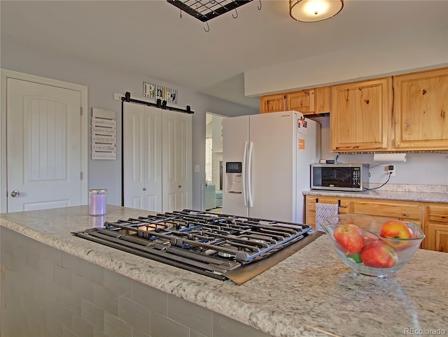 4506 Winewood Village Dr, Colorado Springs, CO 80917 - kitchen featuring white fridge with ice dispenser, gas cooktop, a barn door, stainless steel microwave, and light stone countertops