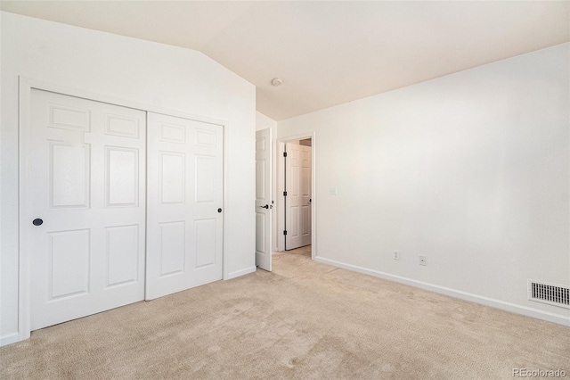 unfurnished bedroom featuring light carpet, a closet, and lofted ceiling