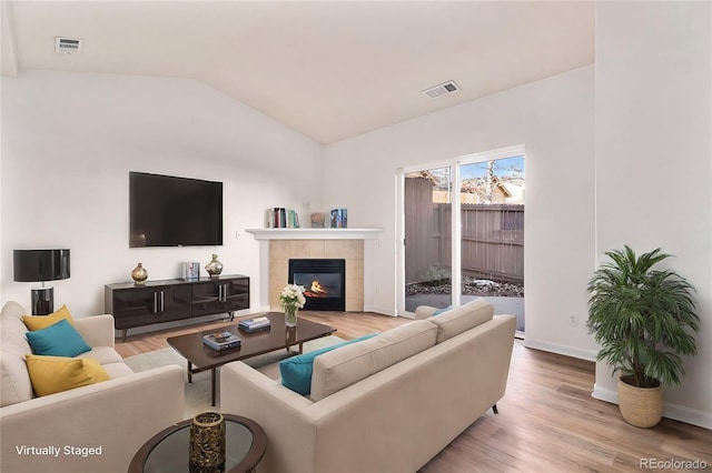 living room with a fireplace, vaulted ceiling, and light wood-type flooring