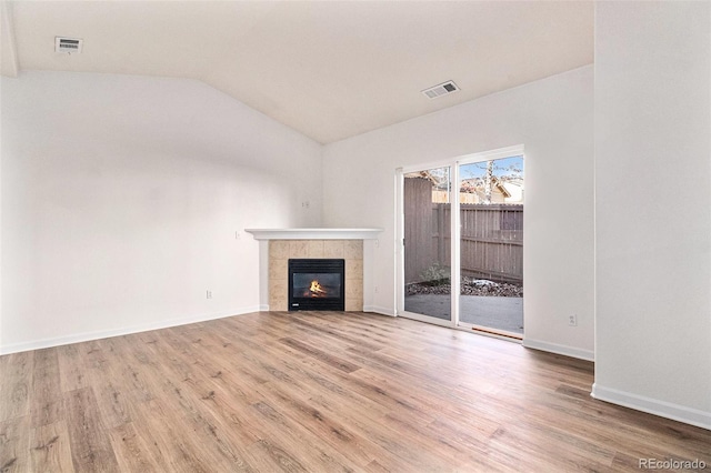 unfurnished living room featuring a tile fireplace, hardwood / wood-style flooring, and lofted ceiling