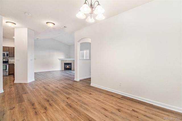 unfurnished living room with a tiled fireplace, a chandelier, lofted ceiling, and light wood-type flooring