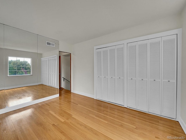 unfurnished bedroom featuring light wood-type flooring, baseboards, visible vents, and multiple closets