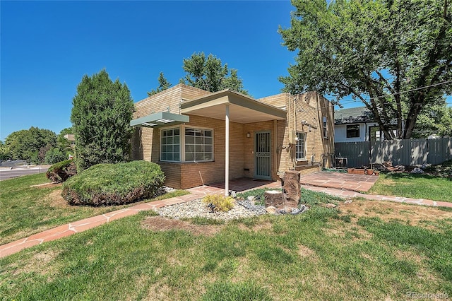 view of front of home with a patio area, brick siding, a front lawn, and fence