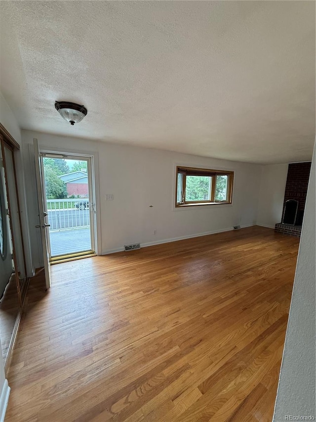 3566 E Fair Pl, Centennial, CO 80121 - unfurnished living room with healthy amount of natural light, light wood-type flooring, a textured ceiling, and a brick fireplace