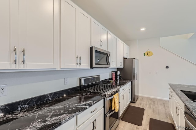 kitchen featuring white cabinets, appliances with stainless steel finishes, light wood-style flooring, dark stone countertops, and recessed lighting