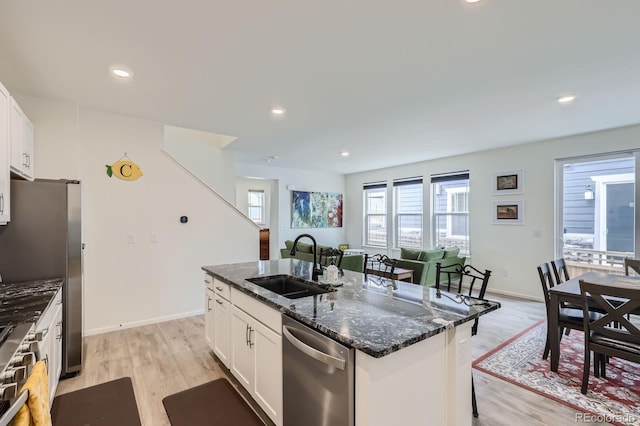 kitchen featuring a sink, dark stone countertops, appliances with stainless steel finishes, and light wood finished floors