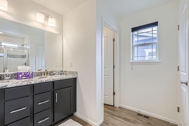 full bathroom with double vanity, visible vents, a shower stall, wood finished floors, and baseboards