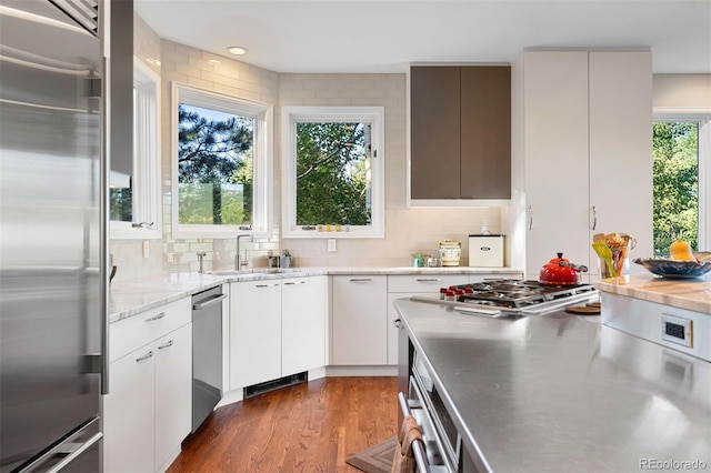 2873 Cortina Ln, Evergreen, CO 80439 - kitchen featuring appliances with stainless steel finishes, stainless steel countertops, decorative backsplash, white cabinetry, and dark wood finished floors