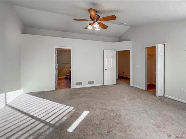 unfurnished bedroom featuring lofted ceiling, ceiling fan, connected bathroom, a walk in closet, and a closet