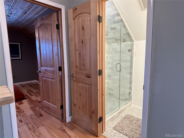 bathroom featuring wood-type flooring, a shower with shower door, and vaulted ceiling