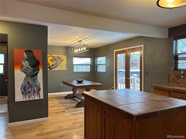 kitchen with tile countertops, tasteful backsplash, hanging light fixtures, light wood-type flooring, and french doors