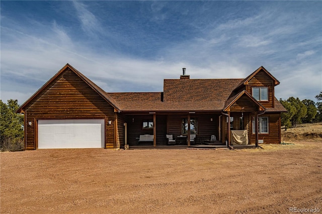 view of front of property featuring driveway, a porch, a shingled roof, a chimney, and a garage