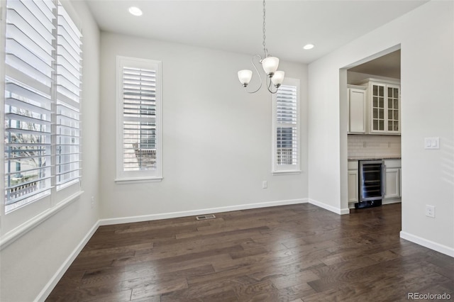 unfurnished dining area with beverage cooler, an inviting chandelier, and dark hardwood / wood-style floors