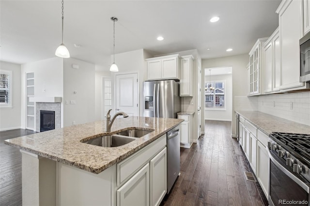 kitchen with sink, stainless steel appliances, decorative light fixtures, white cabinetry, and a kitchen island with sink