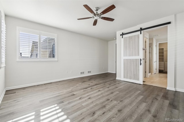 unfurnished bedroom with hardwood / wood-style flooring, ceiling fan, a barn door, and a spacious closet