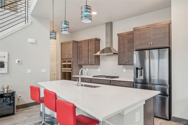 kitchen with decorative light fixtures, sink, a kitchen breakfast bar, stainless steel appliances, and wall chimney exhaust hood