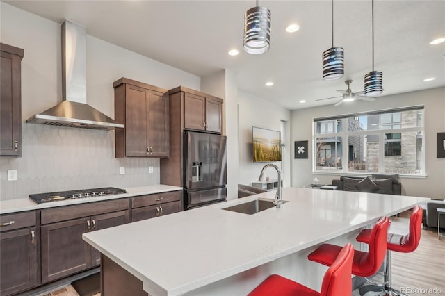 kitchen featuring an island with sink, sink, a kitchen bar, stainless steel appliances, and wall chimney exhaust hood