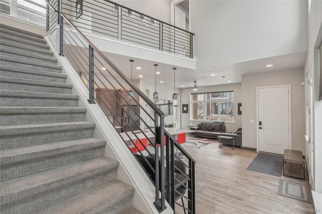 stairway with a towering ceiling, hardwood / wood-style floors, and ceiling fan