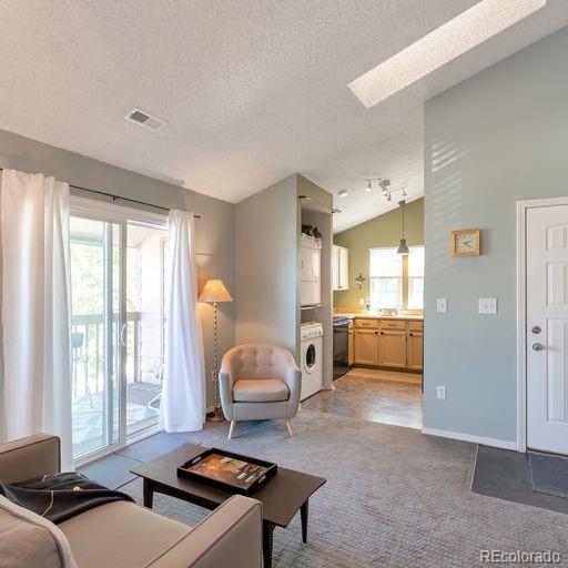living room with plenty of natural light, a textured ceiling, lofted ceiling, a skylight, and estacked washer and dryer