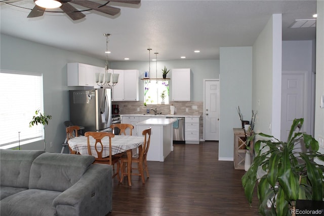 kitchen with appliances with stainless steel finishes, light countertops, a kitchen island, backsplash, and dark wood-type flooring