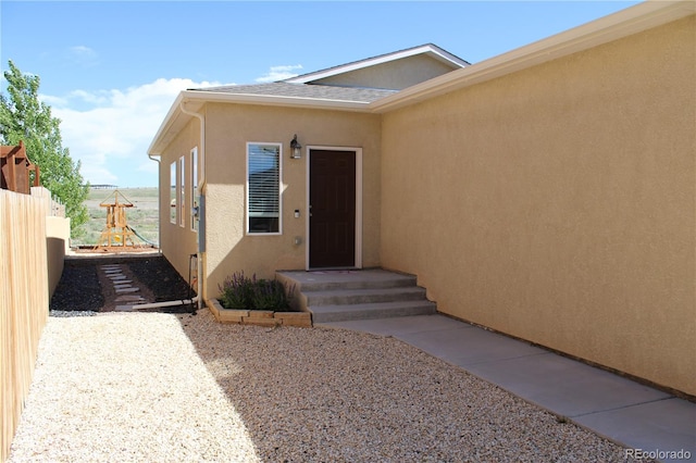 view of exterior entry with fence and stucco siding
