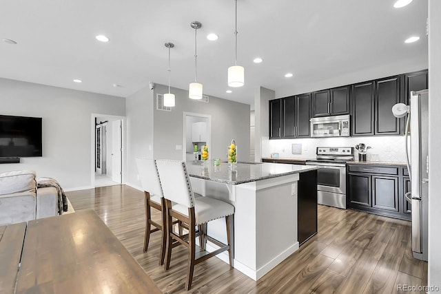 19210 E Pacific Pl, Aurora, CO 80013 - kitchen featuring stainless steel appliances, wood finished floors, a kitchen island, open floor plan, and light stone countertops