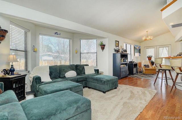 living room with an inviting chandelier, wood finished floors, vaulted ceiling, and visible vents