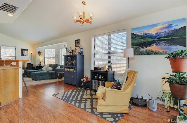 living area with a notable chandelier, lofted ceiling, wood finished floors, and visible vents