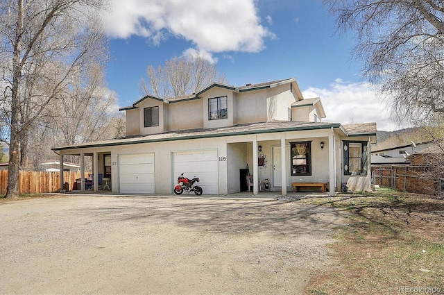 view of front of house featuring stucco siding, fence, driveway, and covered porch
