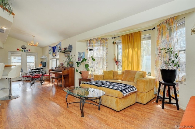 living room with visible vents, vaulted ceiling, a notable chandelier, and light wood finished floors