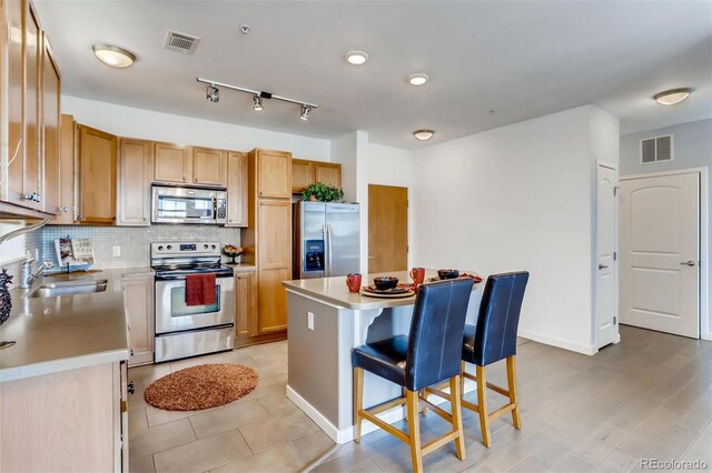 13456 Via Varra Unit 315, Broomfield, CO 80020 - kitchen with appliances with stainless steel finishes, a breakfast bar, light countertops, a kitchen island, and backsplash